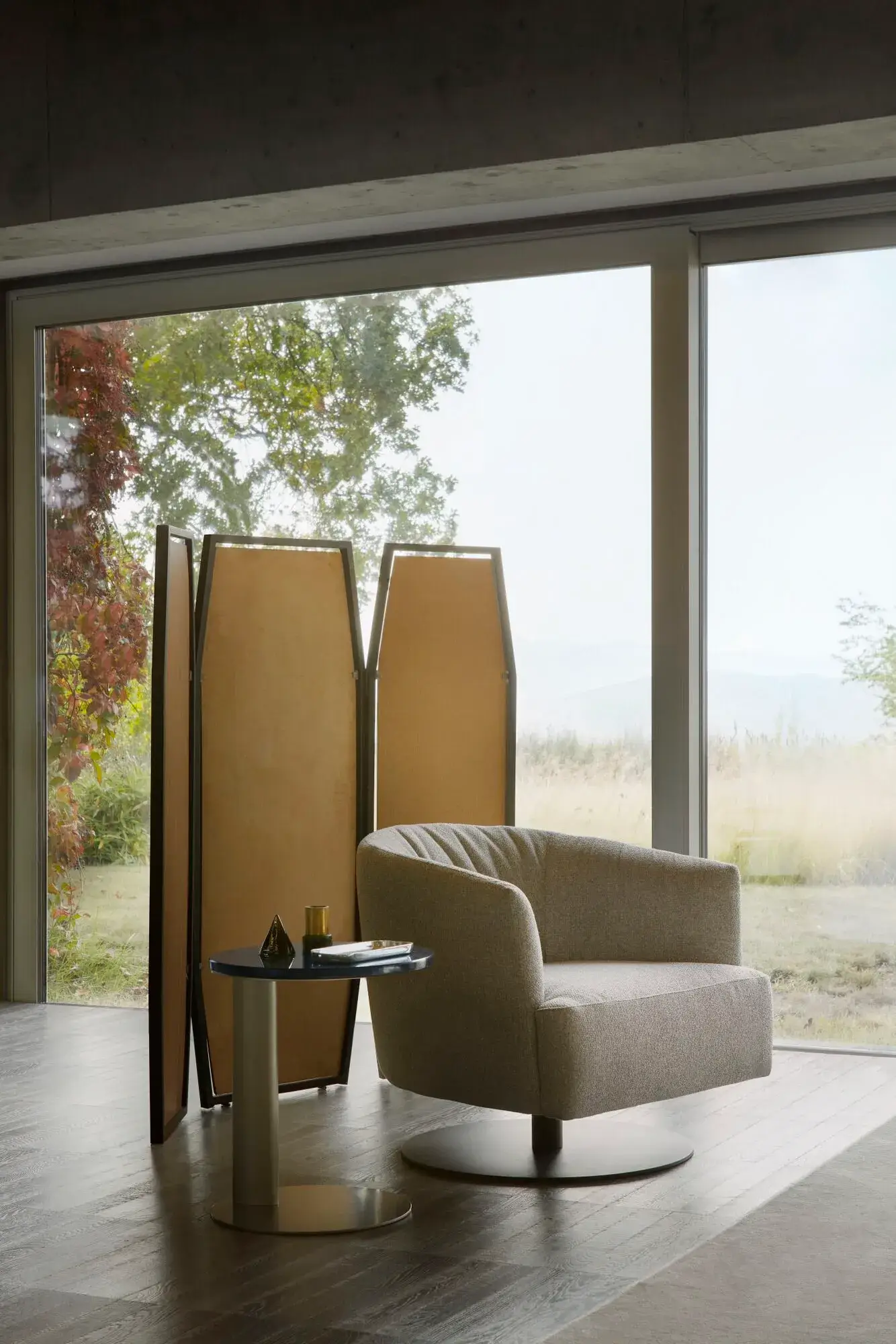 gray snug looking circular swivel arm chair on round black base in an empty room with large windows
